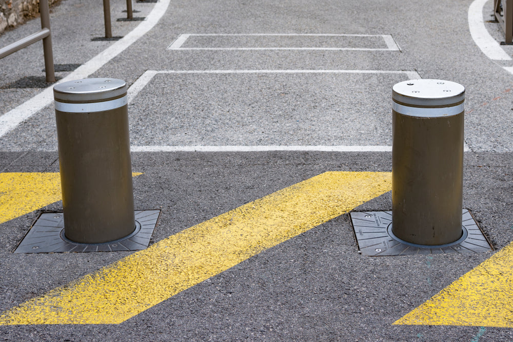 Two retractable bollards installed on a road with yellow painted markings.