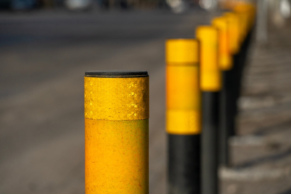 Row of yellow and black bollards along a roadside, with the front one in focus.
