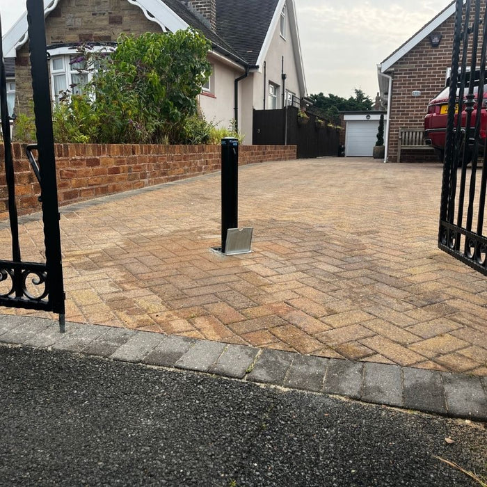 Ramco 600 telescopic driveway security bollard in block paved driveway behind of metal gates.