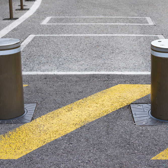 Two retractable bollards installed on a road with yellow painted markings.