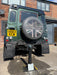Ramco 600 black telescopic security bollard protecting a Land Rover Defender on a residential driveway — wider angle view