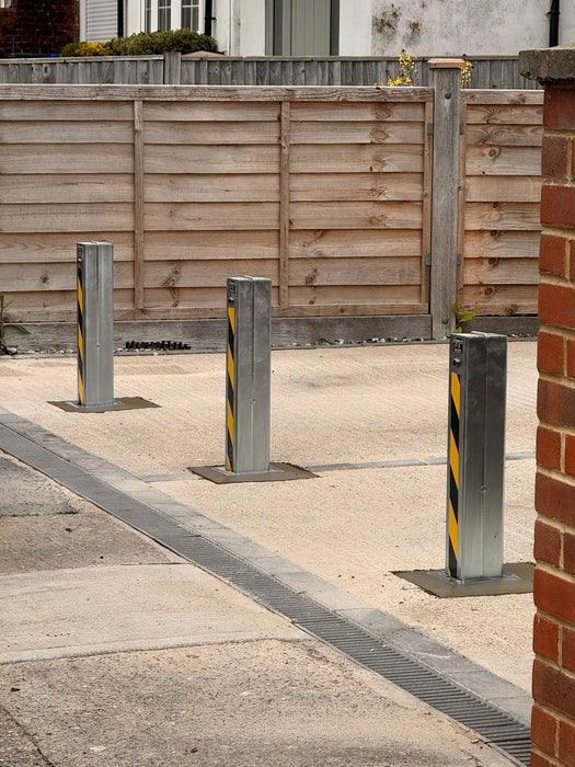 Three Ramco 100 galvanised telescopic security bollards with hi-vis tape installed in a row across a resin-bound driveway entrance