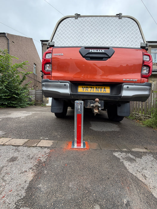 Ramco 100 telescopic security bollard with red reflective tape installed behind a Toyota Hilux Invincible on a residential driveway