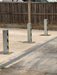 Three Ramco 100 telescopic security bollards with hi-vis chevron tape securing a wide driveway entrance — alternative angle view