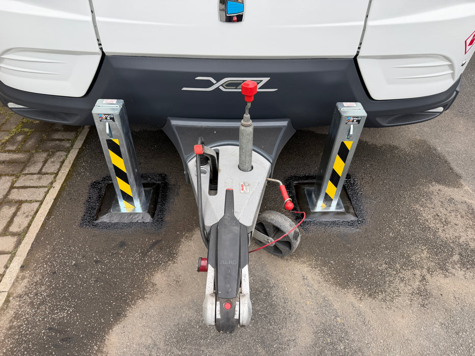 Two Ramco 100 telescopic security bollards with hi-vis tape flanking a Coachman Xcel caravan tow hitch for caravan theft protection