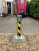 Ramco 100 telescopic security bollard with hi-vis tape freshly installed in concrete on a gravel driveway — close-up of base plate installation